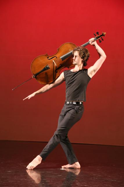 Joseph Teeter on a red stage holding a cello in a dance pose. 